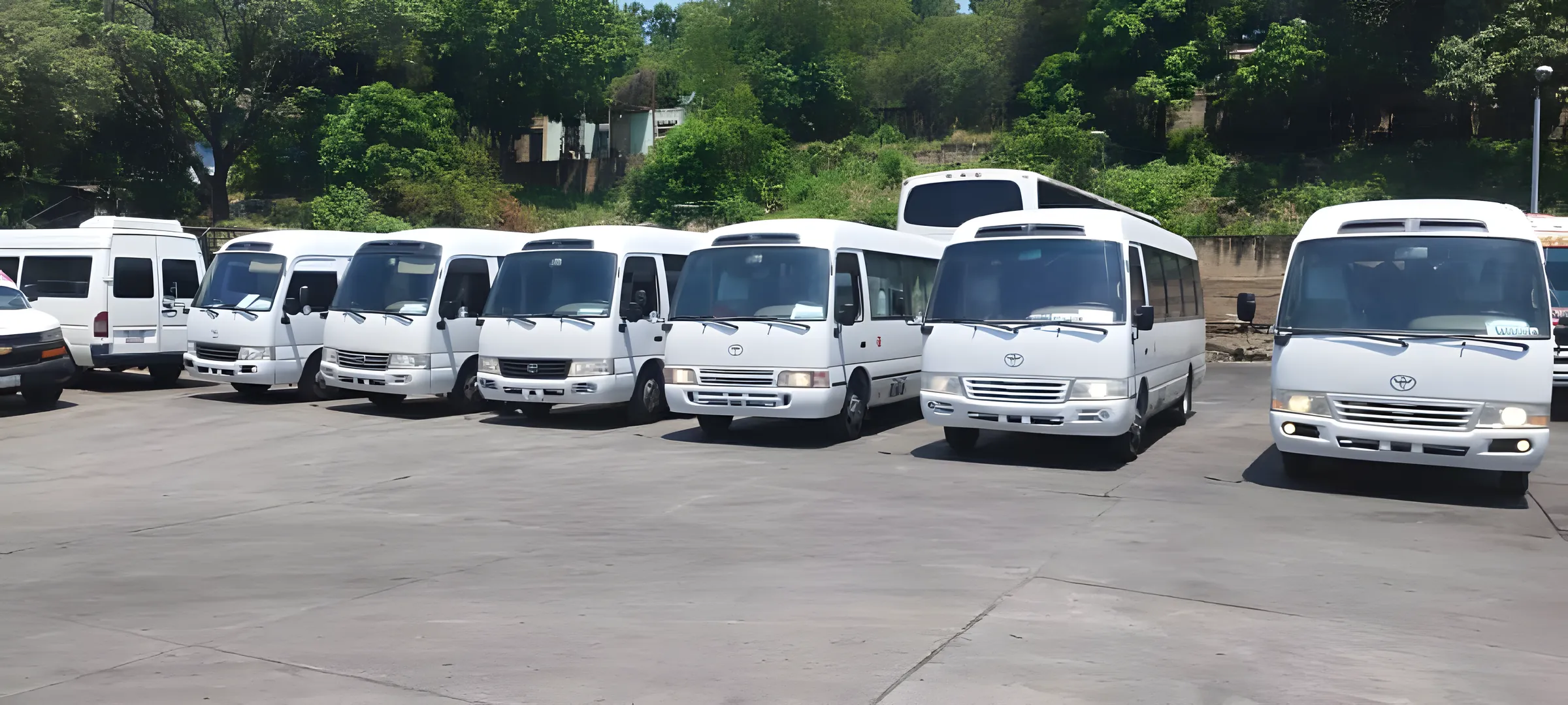 Fila de minibuses y vans blancos de la flota de ACT estacionados en el patio.
